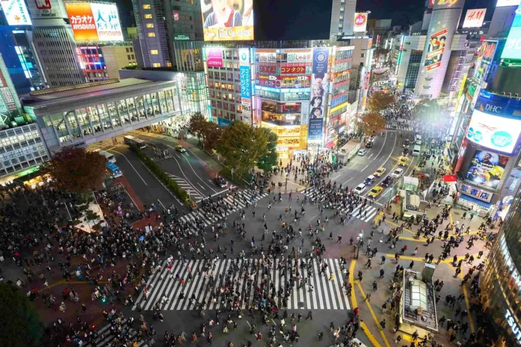 Shibuya Crossing at night, illuminated by city lights with crowds of people.