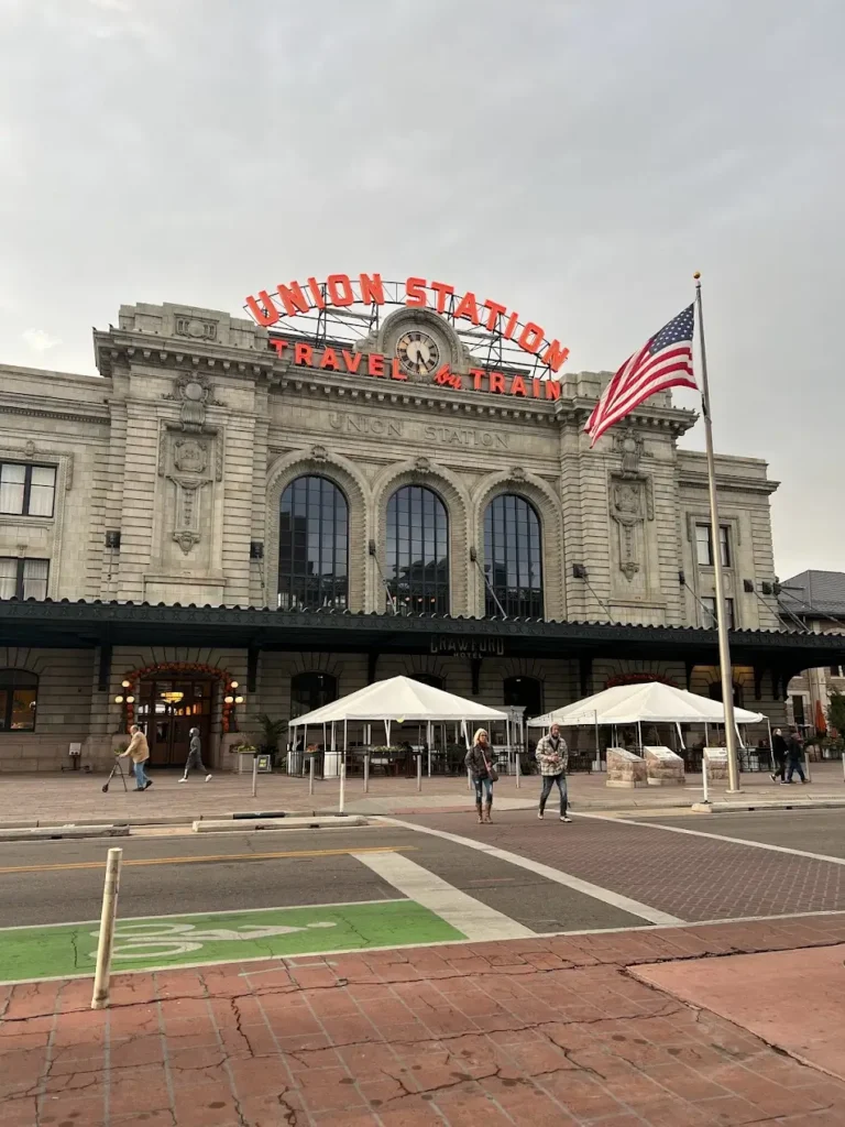 Denver Historic Union Station building with "Travel by Train" sign and American flag Transit-Oriented Development