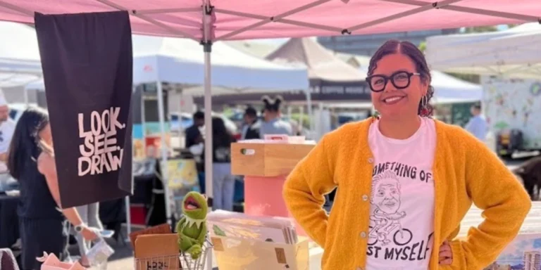 Look See Draw artiest Aileen Martinez in front of her booth with a banner that has Look See Draw on it. There is also her son kermit in the picture.